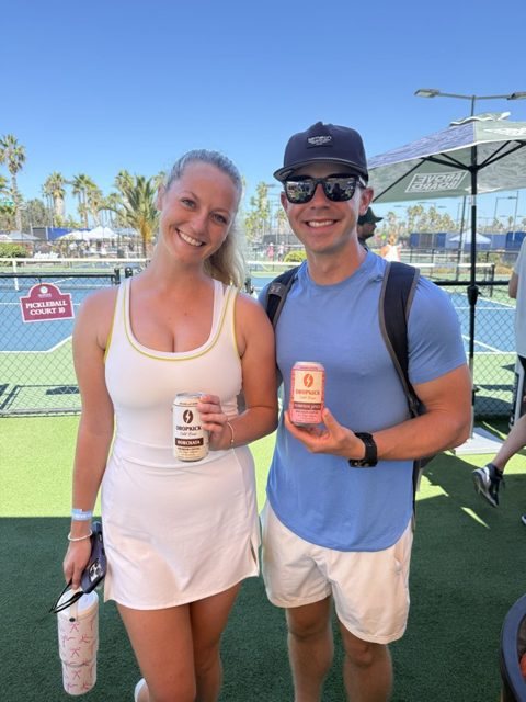 Two friends at the tennis courts holding DropKick cans